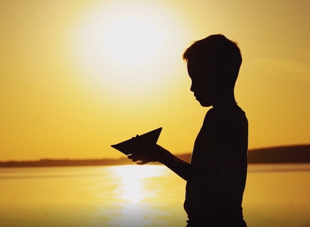 小男孩在夕阳下的湖边折纸船